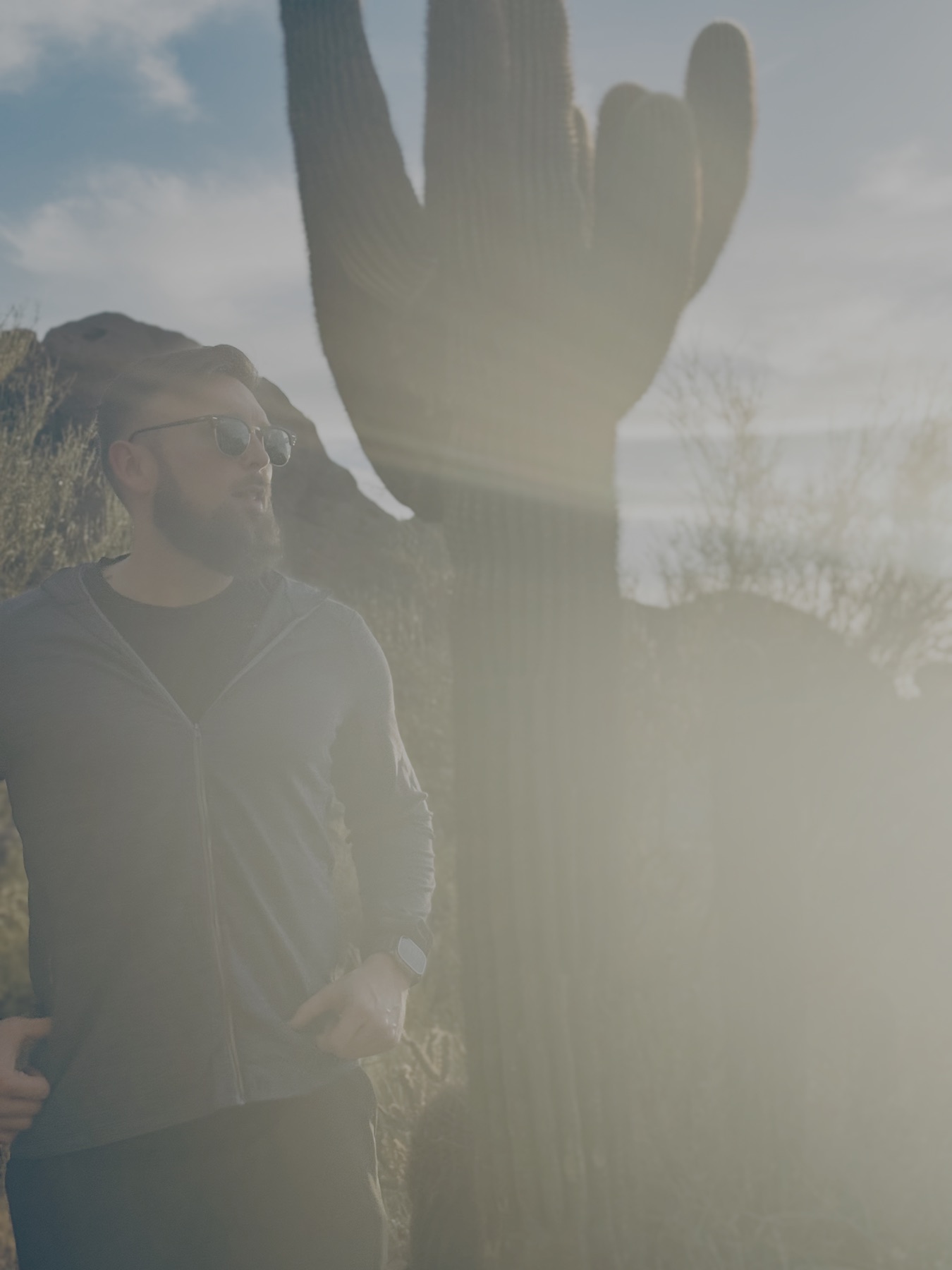 Nathan Haynes standing beside a tall saguaro cactus in the desert